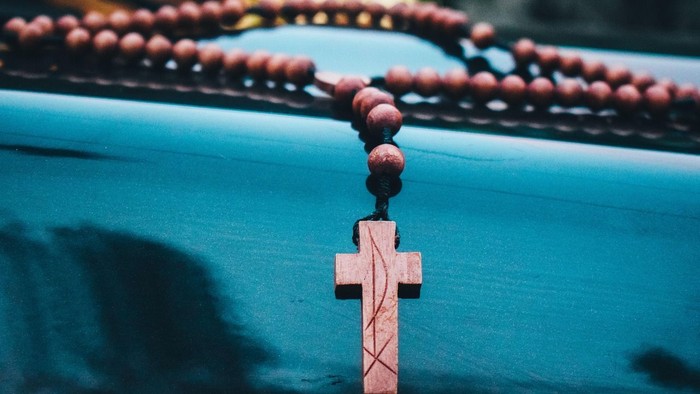 Ein hölzernes Kreuz, das an einer Rosenkranzkette befestigt ist, liegt auf einer reflektierenden blauen Oberfläche.