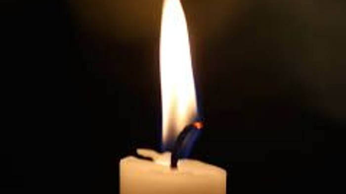 Et tændt lys flammer klart mod en mørk baggrund på et hvidt tællelys.