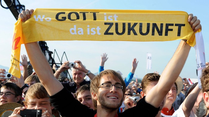 Begeisterte Menge hält ein Banner mit der Aufschrift „Wo Gott ist, da ist Zukunft“ und feiert enthusiastisch.