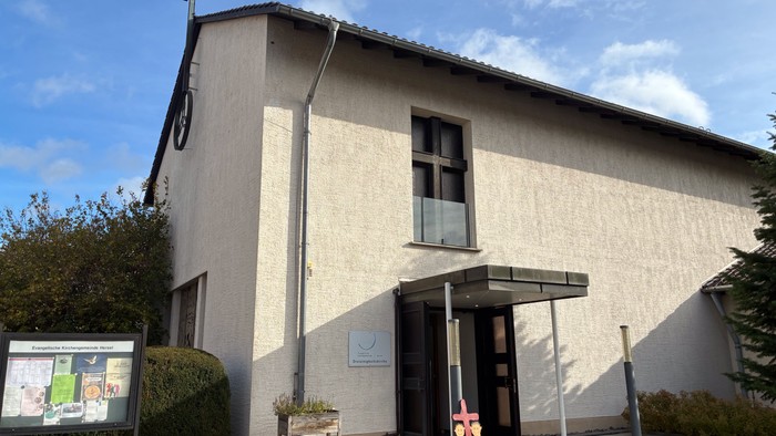 Moderner Kirchenbau mit Kreuz auf dem Dach, Eingangsüberdachung und Außeninformationsdisplay.