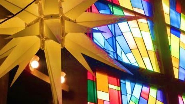 Leuchtende Papiersterne vor buntem Kirchenfenster
