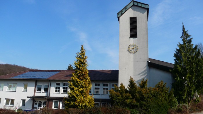 Kirchturm mit Uhr und Kreuz, umgeben von Bäumen und Häusern