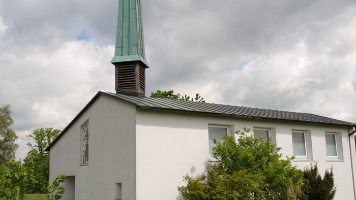 Weiße Kirche mit hohem grünem Turm auf grasigem Hügel.