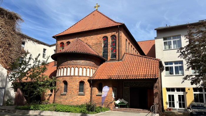 Historische Backsteinkirche mit rotem Ziegeldach und Bogenfenstern in einem malerischen städtischen Umfeld.