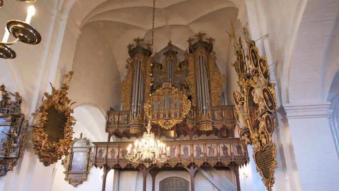 Elegant kirkeinteriør med prægtigt pibeorgel og træbænke under hvælvede lofter.