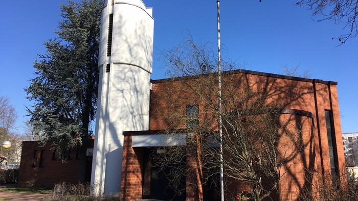 Das Bild zeigt eine Kirche mit hohem Turm und rotem Backsteingebäude unter blauem Himmel.