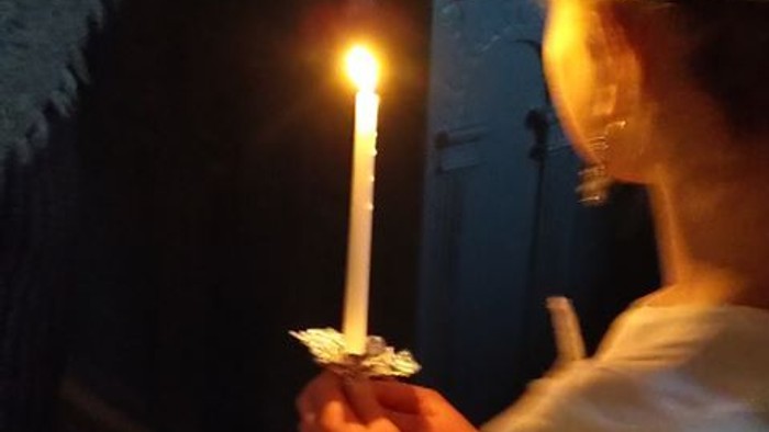 En person holder en lysende stearinlys i mørke omgivelser.