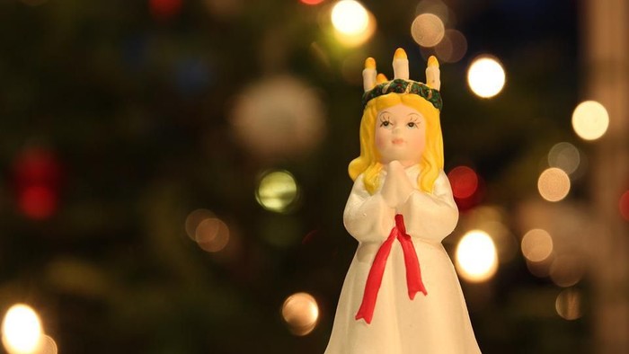 En lille pige med blond hår og en kron med lys foran en juletree.