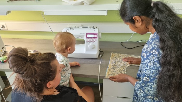 Eine Frau zeigt einer anderen Frau und einem Baby Stoffmuster in einem Nähzimmer.