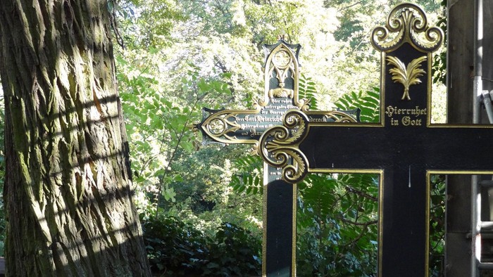 Ein großes, verziertes Kreuz steht im Freien mit einem Baum und einem Gebäude in der Nähe.