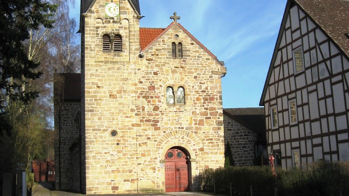 Historische Steinkirche mit hohem Kirchturm und angrenzendem traditionellem Fachwerkhaus.