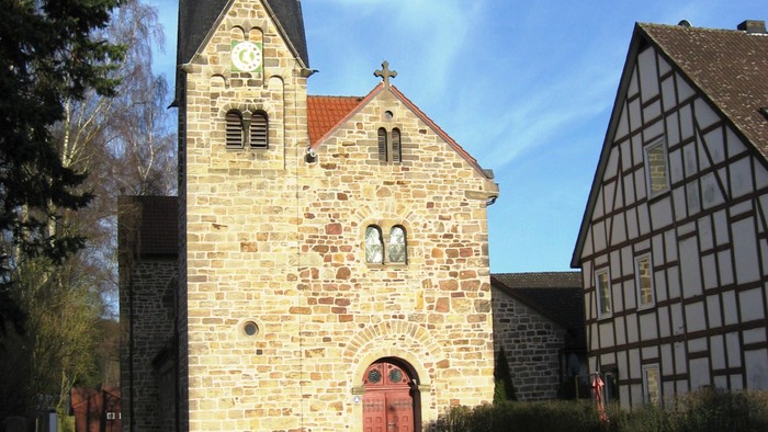 Historische Steinkirche mit hohem Kirchturm und angrenzendem traditionellem Fachwerkhaus.