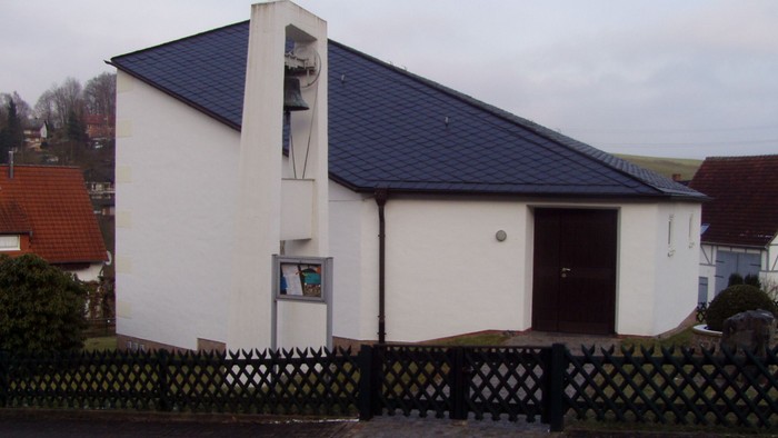 Außenansicht der evangelischen Kirche in Knickhagen. Weiß verputztes Gebäude mit schrägem Dach und freistehendem Glockenturm.