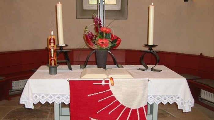 Kirchenaltar mit Kreuz, Kerzen und rotem Tuch mit Taube.