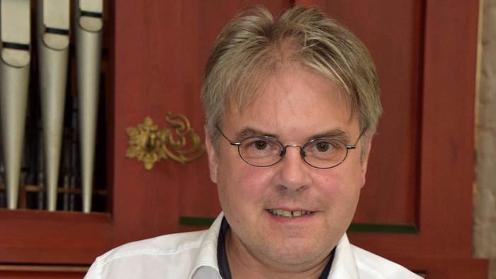 Mann mit Brille sitzt vor Kirchenorgel