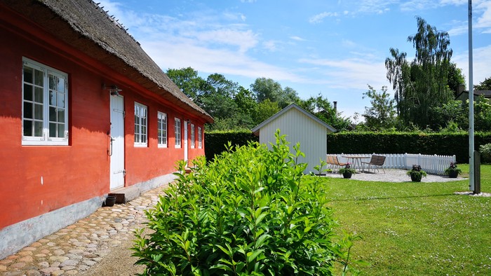 Rødt hus med grønne buske og klædehæng.