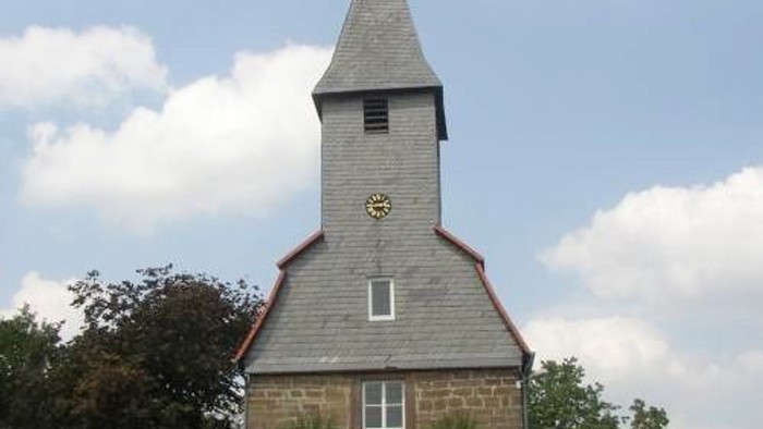 Außenansicht der evangelischen Kirche in Leckringhausen. Kleines Natursteingebäude mit hohem, schieferverkleidetem Turm und spitzem Dach.