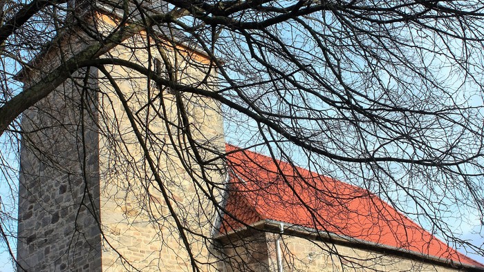 Außenansicht der evangelischen Kirche in Wenigenhasungen. Natursteingebäude mit rotem Ziegeldach und quadratischem Turm.