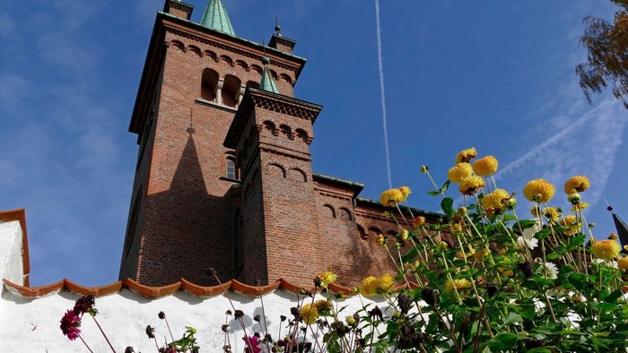 Historisk murstenskirketårn indrammet af livlige gule blomster under en klar blå himmel.