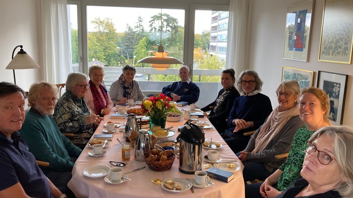 En gruppe af ældre personer sidder til middag i et lysligt og rummeligt stue.