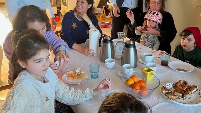 Familien samles omkring et bord og nyder et måltid med forskellige retter og drikkevarer.