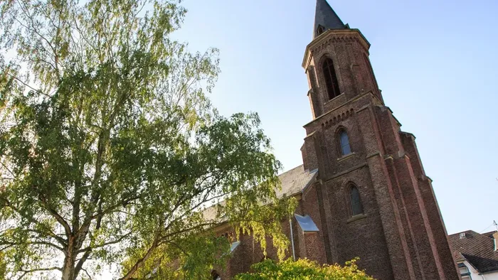 Historische Backsteinkirche mit hohem Turm, umgeben von üppigem Grün unter klarem Himmel.