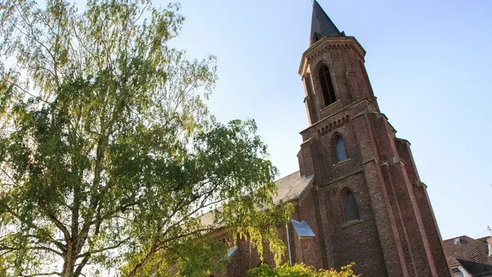 Historische Backsteinkirche mit hohem Turm, umgeben von üppigem Grün unter klarem Himmel.