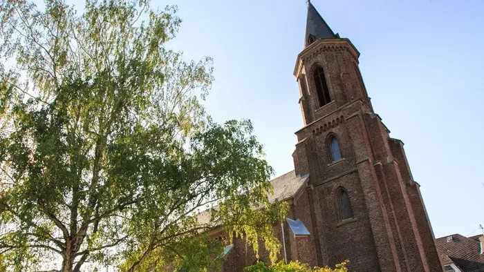 Historische Backsteinkirche mit hohem Turm, umgeben von üppigem Grün unter klarem Himmel.