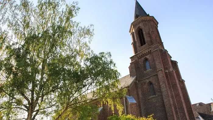 Historische Backsteinkirche mit hohem Turm, umgeben von üppigem Grün unter klarem Himmel.