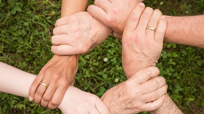 Eine Gruppe von Menschen, die sich im Kreis an den Händen halten und Einheit und Teamwork im Freien symbolisieren.