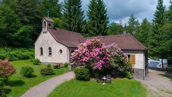 Idyllische Kapelle, umgeben von blühenden Sträuchern und üppigem Grün in einer ruhigen ländlichen Umgebung.