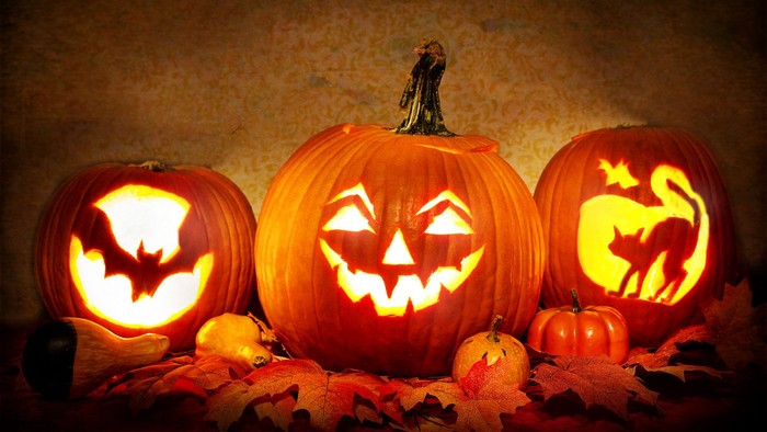 Tre udskårene pumpker med grusomme ansigter og en lille figur på den midterste.