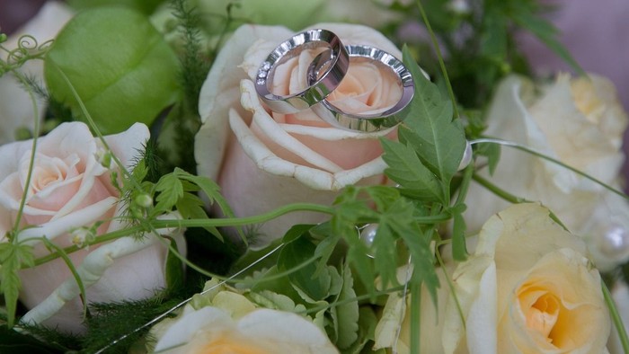 Ein Paar Ringe liegt auf einer Blumenanordnung aus weißen und gelben Rosen