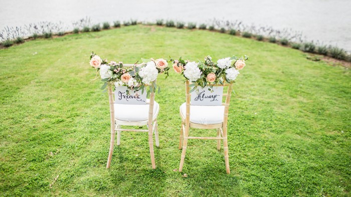 Elegante Hochzeitsstühle, geschmückt mit Blumenarrangements und herzlichen Botschaften auf einem üppigen grünen Rasen.