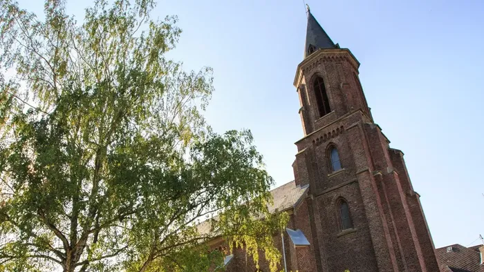 Historische Backsteinkirche mit hohem Turm, umgeben von üppigem Grün unter klarem Himmel.