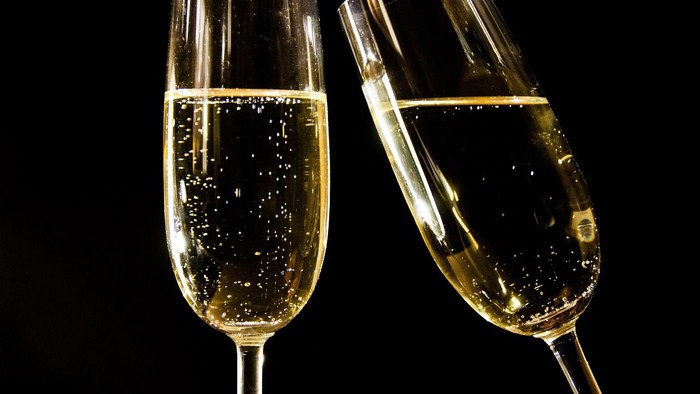 Zwei Champagnergläser mit prickelndem Getränk vor schwarzem Hintergrund