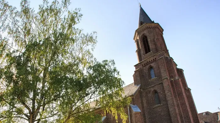 Historische Backsteinkirche mit hohem Turm, umgeben von üppigem Grün unter klarem Himmel.