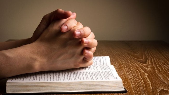 Hands folded in prayer on top of an open bible