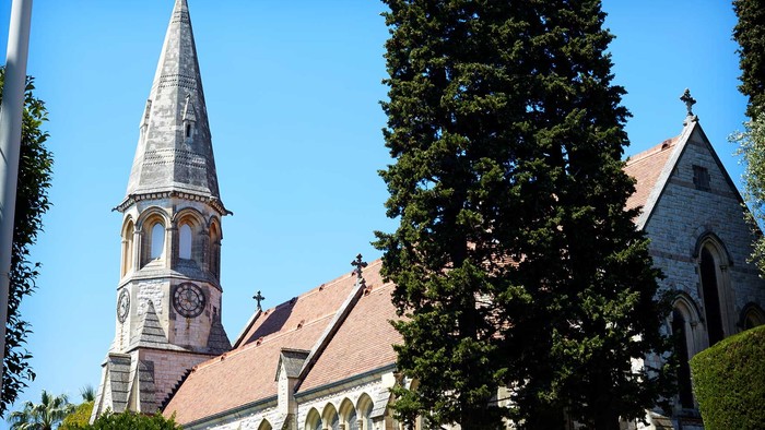 En kirke med spir med tårn og klokke, omgivet af træer og buske