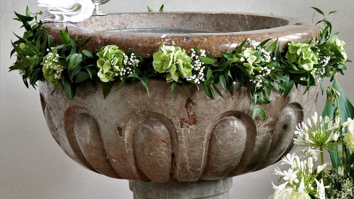 Ein großer Terrakotta-Waschtrog, der mit weißen Blumen und grünen Blättern geschmückt ist, mit einer weißen Taube darauf