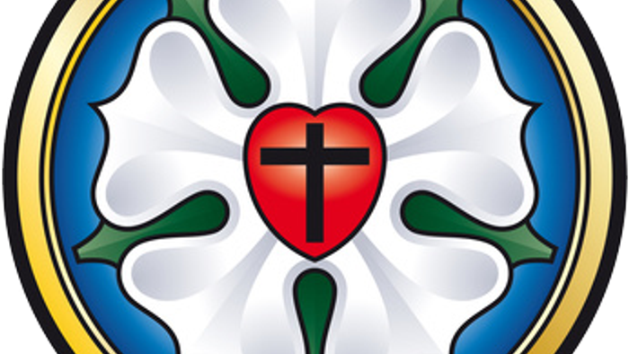 Das Bild zeigt ein weißes Lilienemblem mit einem roten Herzen und Kreuz in der Mitte, umgeben von grünen Blättern und einem blauen Kreis.