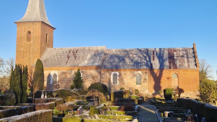 En kirke med tårn og en have med buske og stier