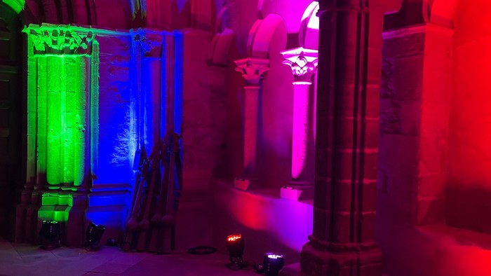 Farbenfrohe Lichtprojektionen erhellen einen architektonischen Innenraum mit gotischen Bögen und Säulen.