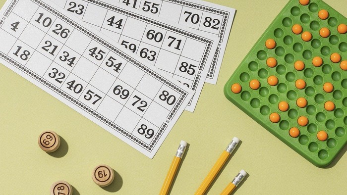 Das Bild zeigt Bingo-Karten, Würfel, Bleistifte und ein grünes Gummibärchen-Spiel.