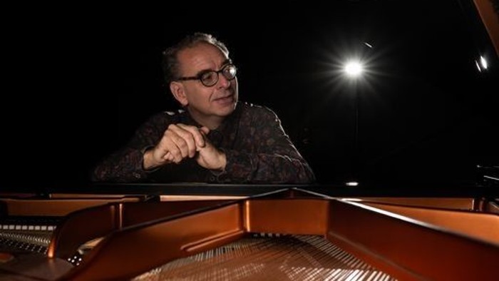 En mand spiller klaver med et koncentreret udtryk under scenenlyset.