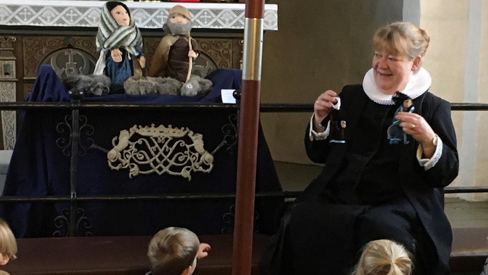 Præsten med dukker i hånden og børn der lytter