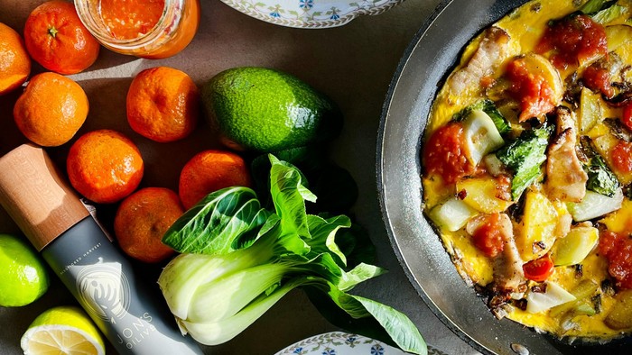 Friske salatbowle, ristede grøntsager og en pande med en bagt ret fyldt med farverige ingredienser på et solbeskinnet bord.