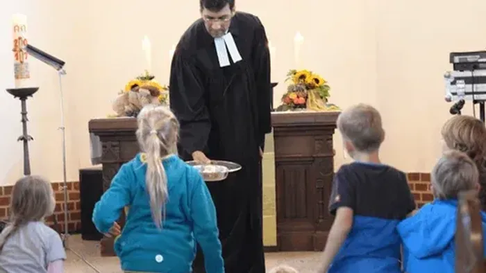 Kinder in Kirchenraum mit Pfarrer und Kerzenarrangement