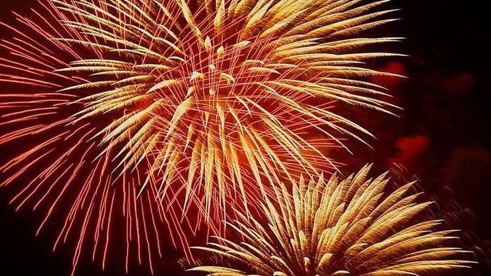 Leuchtende Feuerwerke explodieren am Nachthimmel und entfalten goldene und rote Farbtöne.