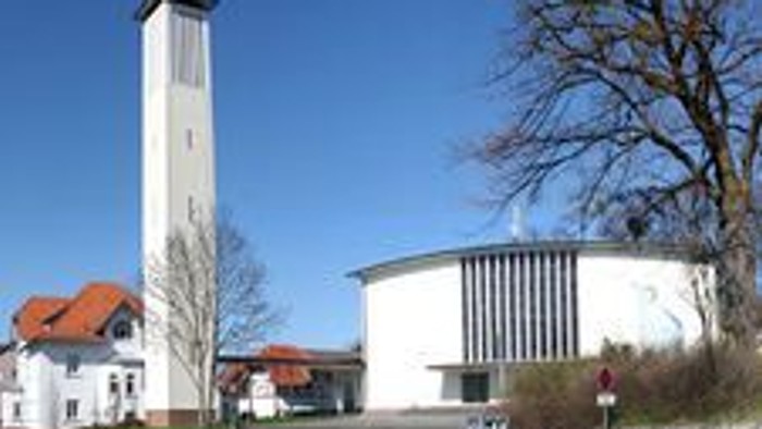 Moderne Kirche mit hohem Glockenturm und runder Kapelle in einer ruhigen, landschaftlich gestalteten Umgebung.